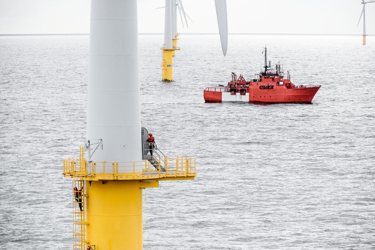 Aerial shot of men working on a wind turbine, with a boat in the background